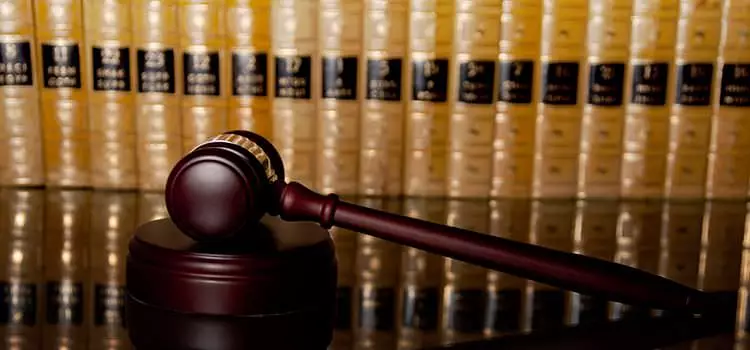 A gavel on top of a polished desk in foreground, neatly stacked legal books in the background.