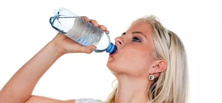A woman quenching her thirst by drinking from a clear plastic bottle of water