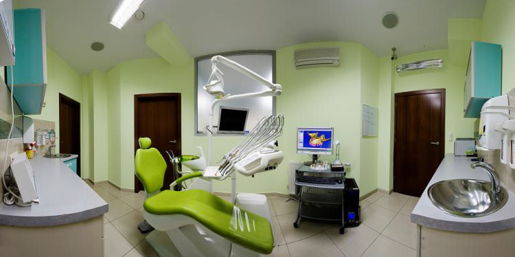A typical dental office room with lime-green chair, a light shade of green wallpaper, and stainless steel sink.