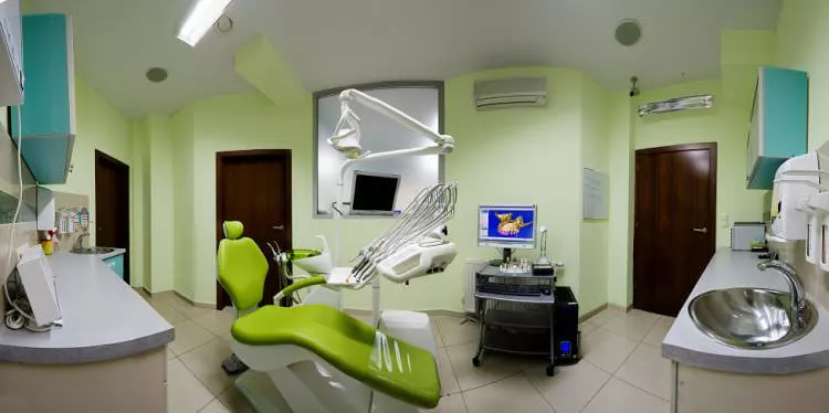 A typical dental office room with lime-green chair, a light shade of green wallpaper, and stainless steel sink.