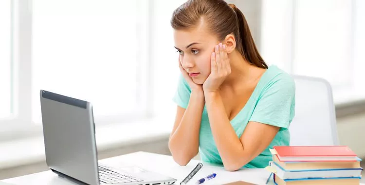 Woman looking at computer with her head resting on her palms.