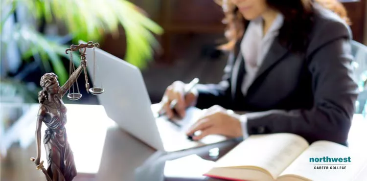 A Female Lawyer working with a laptop in background, and lady justice statue on desk in foreground.