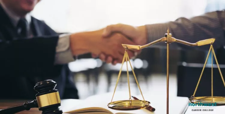 A man shaking hand with another man in background, with gavel and scale in foreground.