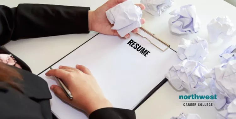 A woman struggling to write her resume, as is evident with several crumpled up papers of her earlier draft.