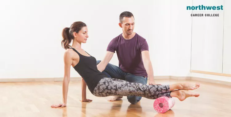 Pilates instructor helping a woman to use a foa, roller.