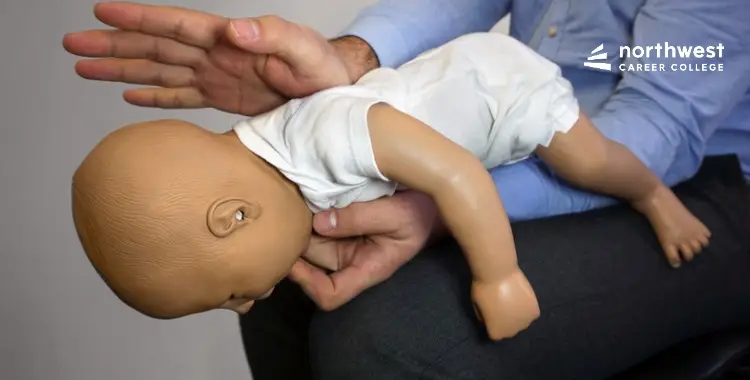 A person demonstrates CPR techniques on a baby mannequin in a training setting.
