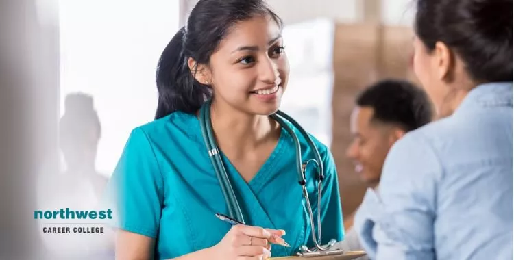 Attentive medical assistant talks with patient as she notes her case history.