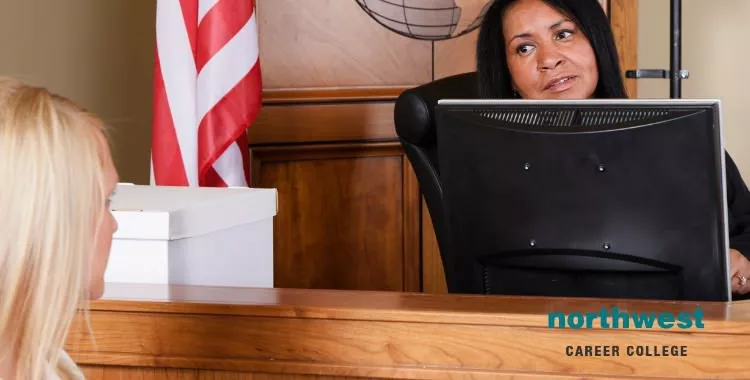 The court room using technology where a female judge is talking with a court clerk.