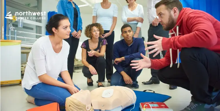 A group of students learns CPR techniques from an instructor using a mannequin in a classroom setting.