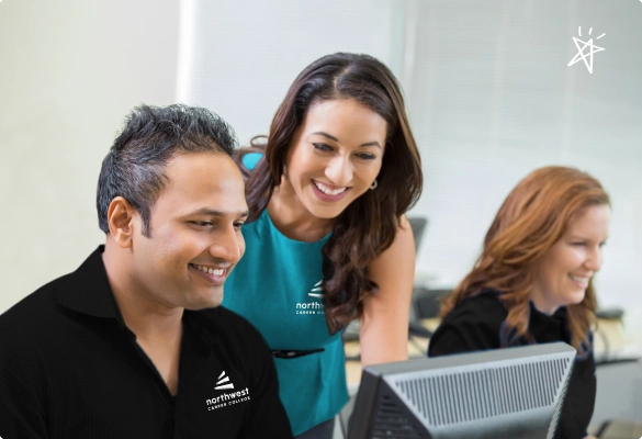Three students engaged in a Las Vegas Trade School Class, collaborating and smiling at a computer screen.