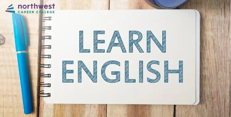 A notebook on a wooden table with LEARN ENGLISH prominently displayed, alongside a blue pen and a cup.