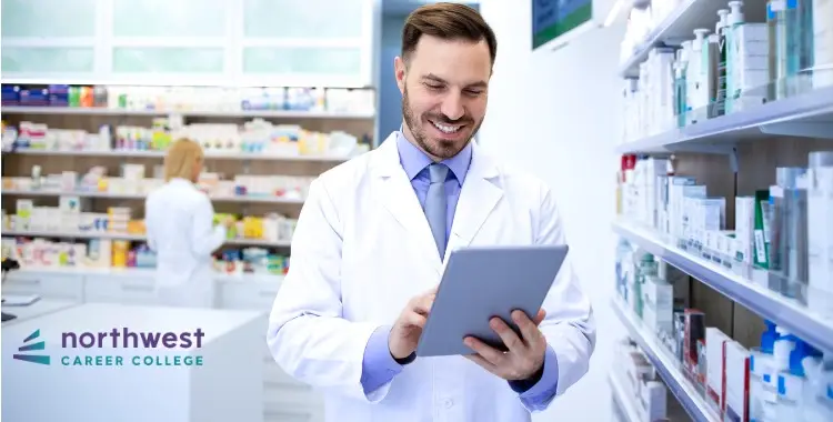A smiling pharmacist in a lab coat uses a tablet in a pharmacy, with shelves of medications in the background.