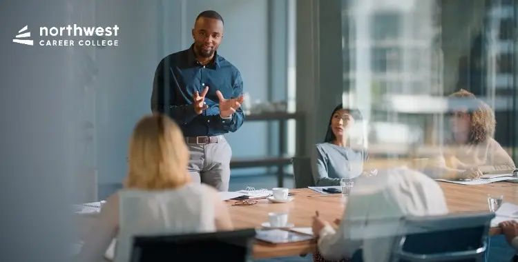 A diverse group in a conference room listens as a man presents at a meeting.