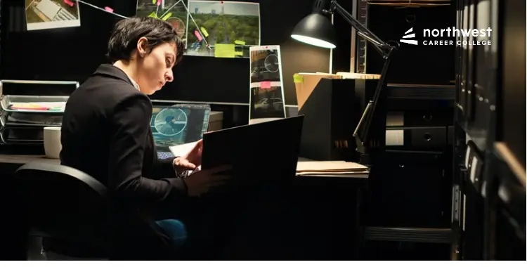 A focused individual reviews documents at a desk, surrounded by files and photographs in a dimly lit office.