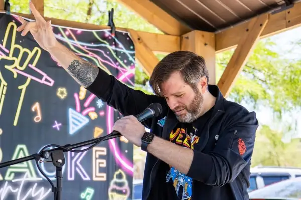 A man with tattoos passionately performs at a microphone under a colorful backdrop.