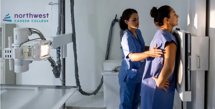 Two women in scrubs in a medical setting, one assisting the other with an X-ray machine.