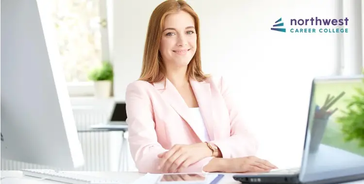 A smiling woman in a pink blazer sits at a desk with a laptop, promoting Northwest Career College.