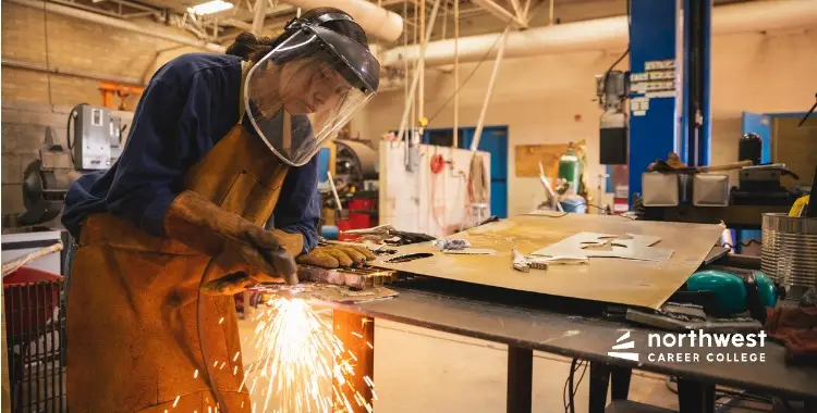 A student in protective gear welds metal, creating sparks in a workshop setting at Northwest Career College.