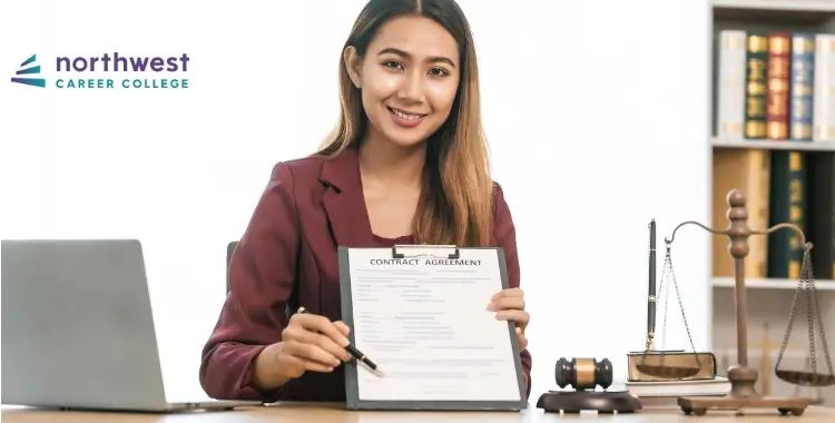 A smiling woman in a suit holds a contract agreement at a desk with legal books and a scale in the background.