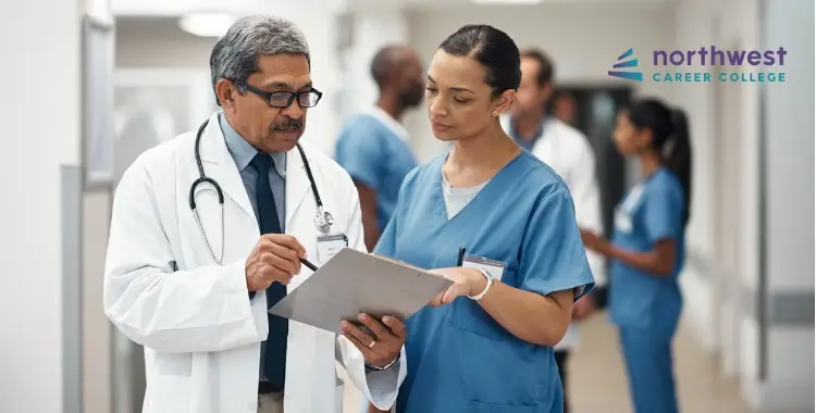 A doctor and nurse discuss patient information in a hospital corridor, with other healthcare professionals in the background.