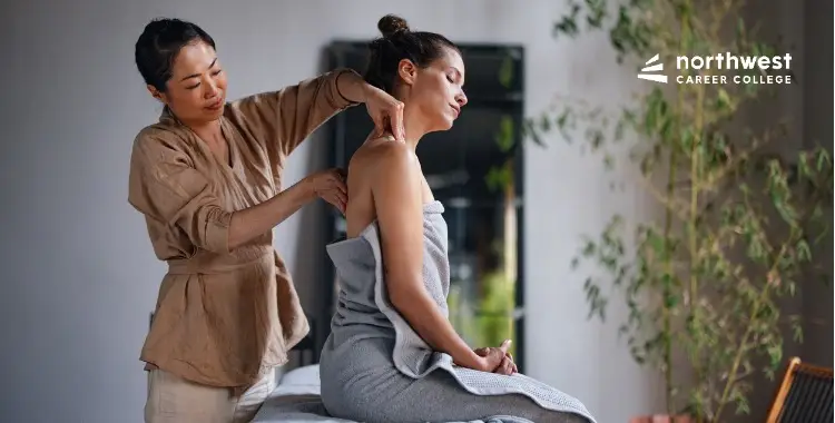 A therapist gives a shoulder massage to a seated client in a serene, indoor setting.