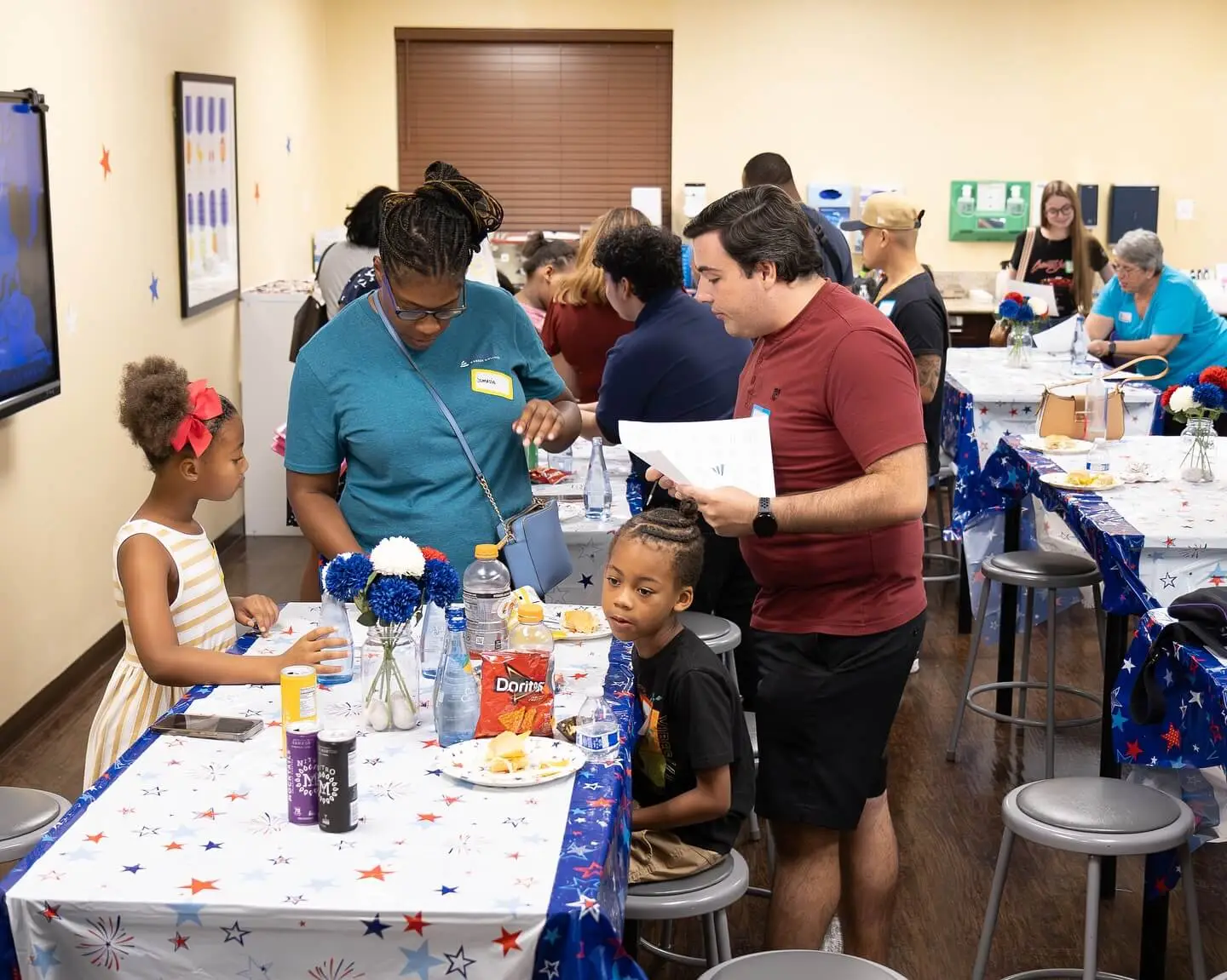A group of people socializing at tables with food and decorations in a festive indoor setting.