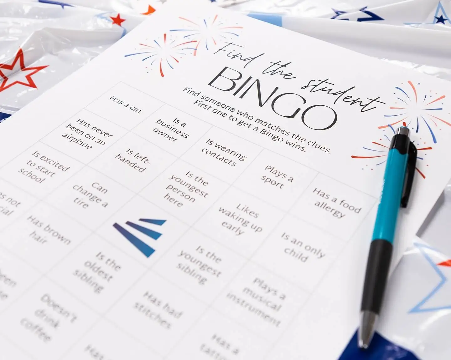 A bingo card titled Find the Student Bingo with various prompts and a pen beside it, set on a festive background.