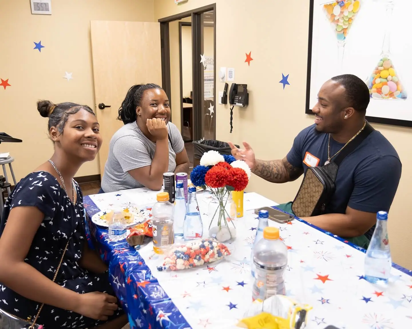 Three people sit at a decorated table, enjoying snacks and drinks while engaged in conversation.