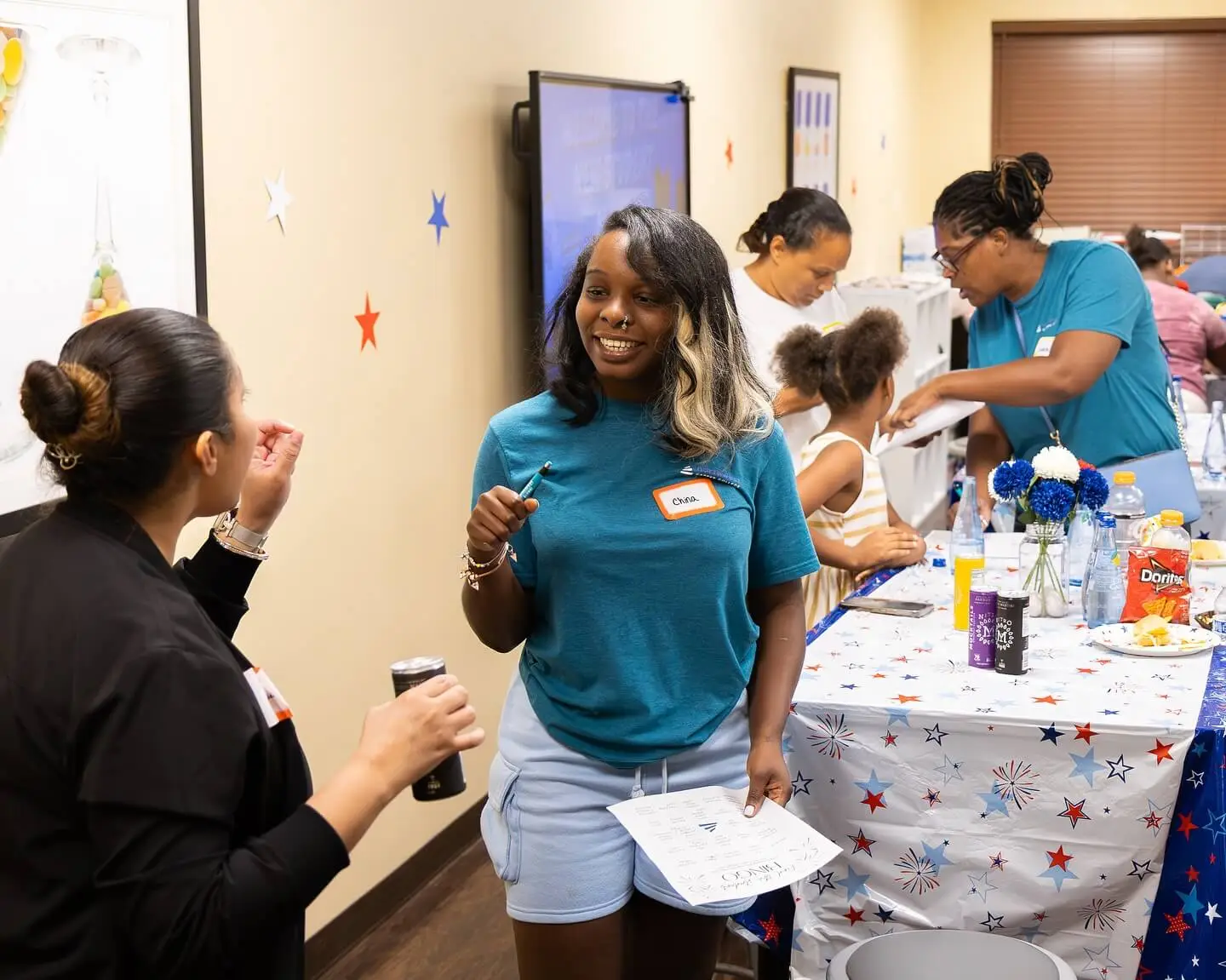 A lively gathering with people chatting, enjoying food, and engaging in activities at a decorated table.