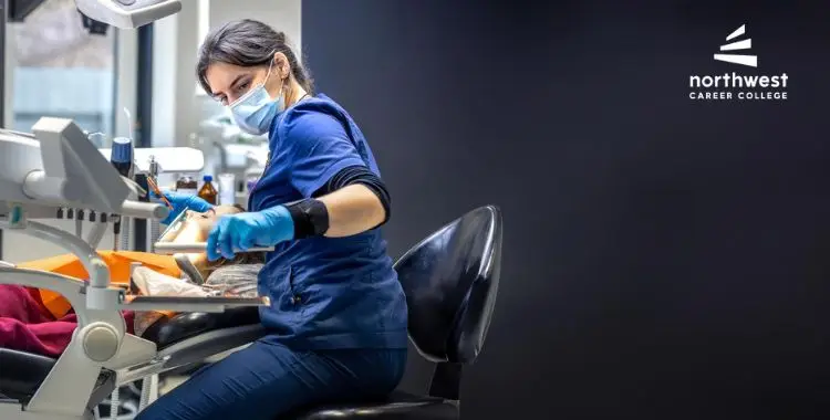 A dental professional in a blue uniform and mask works on a patient in a modern dental office.