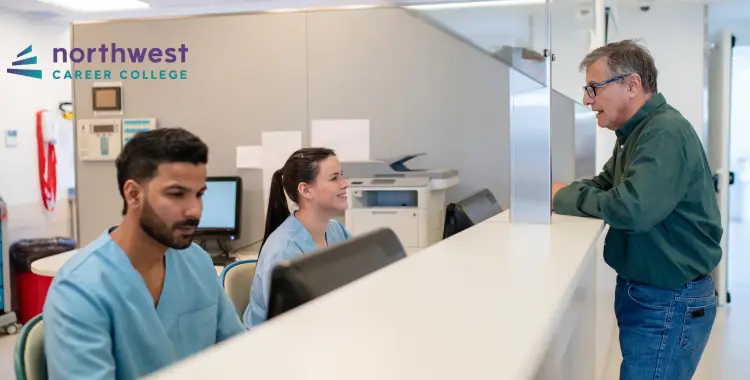Two healthcare students in scrubs assist a man at a reception desk in a modern office setting.