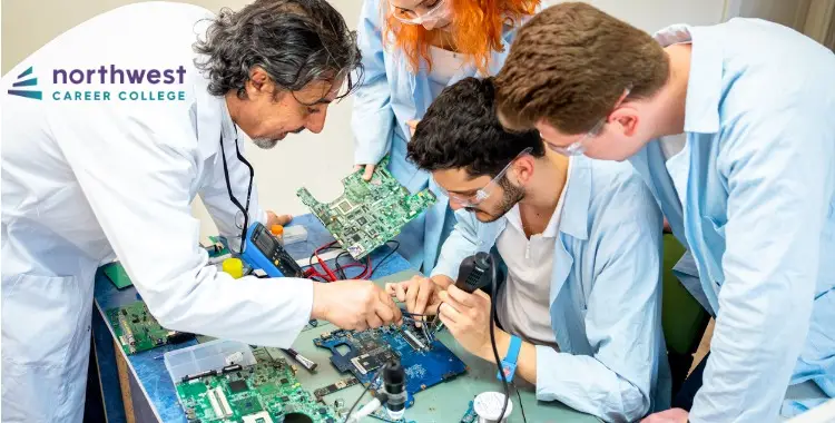 Students and an instructor work together on circuit boards at a table, focused on electronics repair.