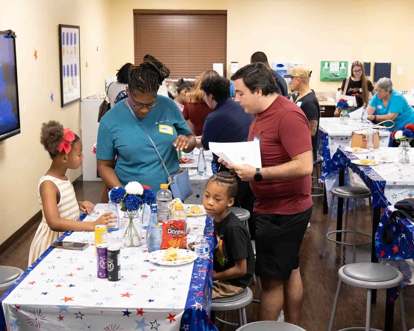A group of people socialize at tables decorated with stars, enjoying food and drinks in a community space.