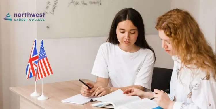 Two students study together at a table with flags of the USA and UK, focused on their books and notes.