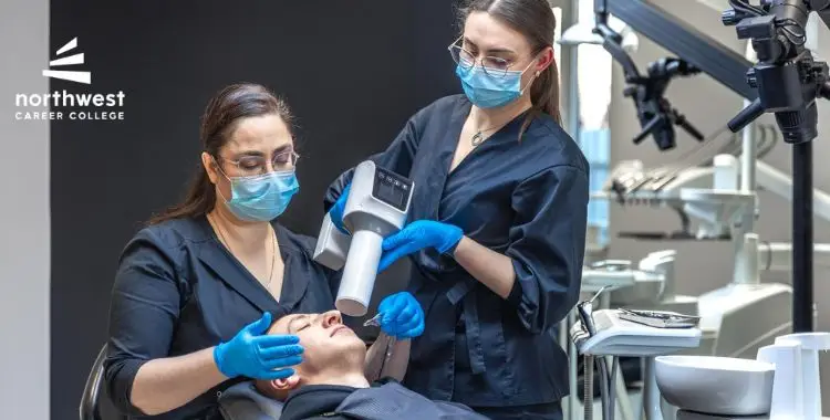 Two dental professionals in masks and gloves work on a patient using a dental device in a clinical setting.