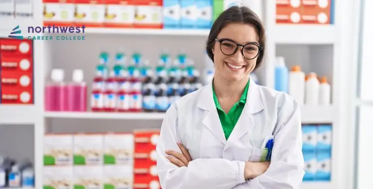 Smiling woman in a lab coat stands with arms crossed in front of colorful shelves filled with bottles and products.