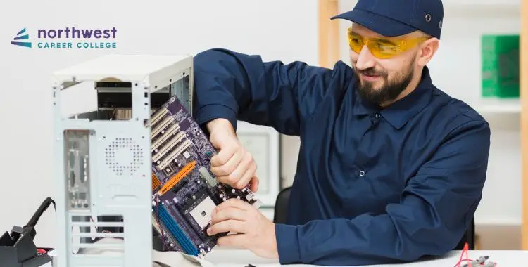 A technician in safety glasses assembles a computer motherboard inside a case at Northwest Career College.