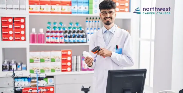 Smiling pharmacist in a lab coat holds a product and scanner, surrounded by shelves of various bottles and boxes.