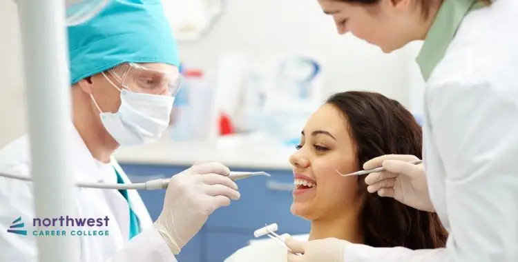 A dentist and assistant examine a smiling patient in a dental office setting.