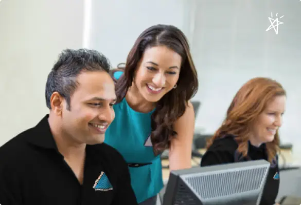 Three colleagues collaborate at a computer, smiling and engaging in a positive work environment.