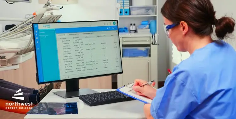 A healthcare professional in scrubs reviews patient data on a computer in a clinical setting.