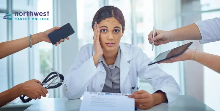 A stressed healthcare professional surrounded by hands holding a phone, tablet, and stethoscope, looking overwhelmed.