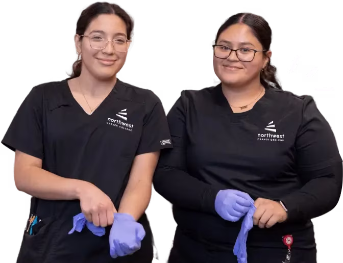Two students at phlebotomy school Las Vegas prepare to put on gloves, smiling and dressed in black scrubs.