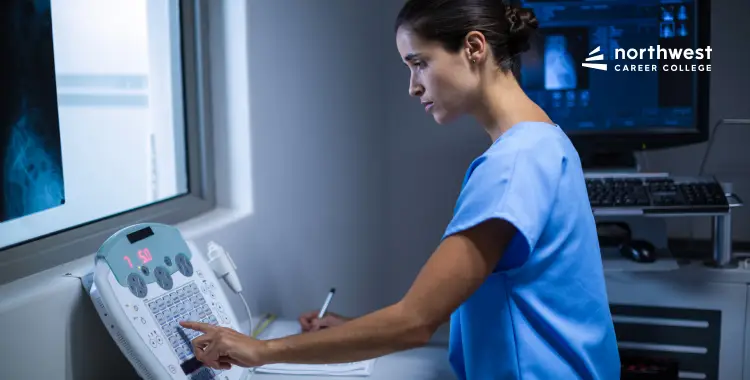 A healthcare professional in scrubs operates a medical device, focused on a screen displaying X-ray images.