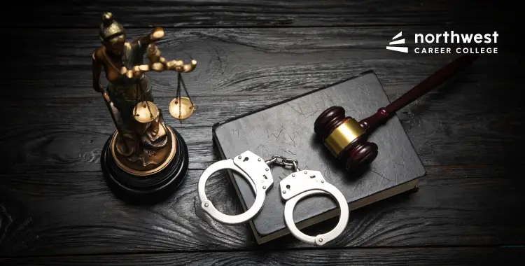 A gavel, handcuffs, a law book, and a statue of Lady Justice on a wooden surface.