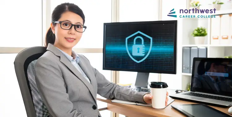 A professional woman sits at a desk with computers, holding a coffee cup, in front of a security-themed screen.