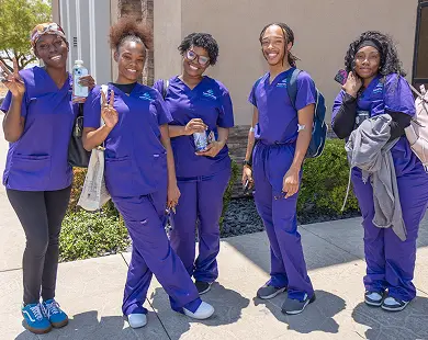 Five students in purple scrubs smile and pose outside, representing the Las Vegas massage school community.