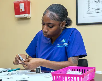 A student in a blue uniform practices skills in a medical assistant training program at a table with supplies.