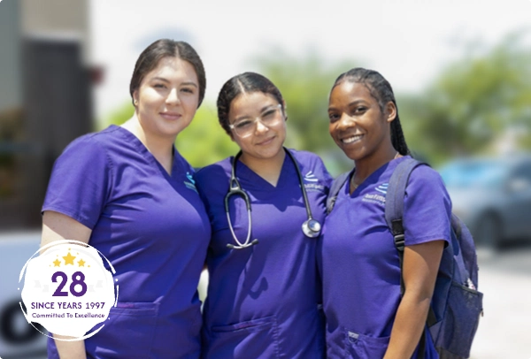 Three women in purple scrubs smile together outdoors, with a badge indicating 28 years of commitment to excellence.