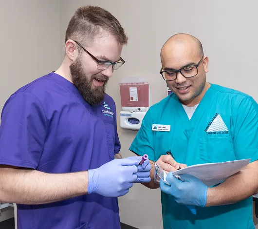 Two instructors review a blood sample during a phlebotomy course in Las Vegas, focusing on proper techniques.